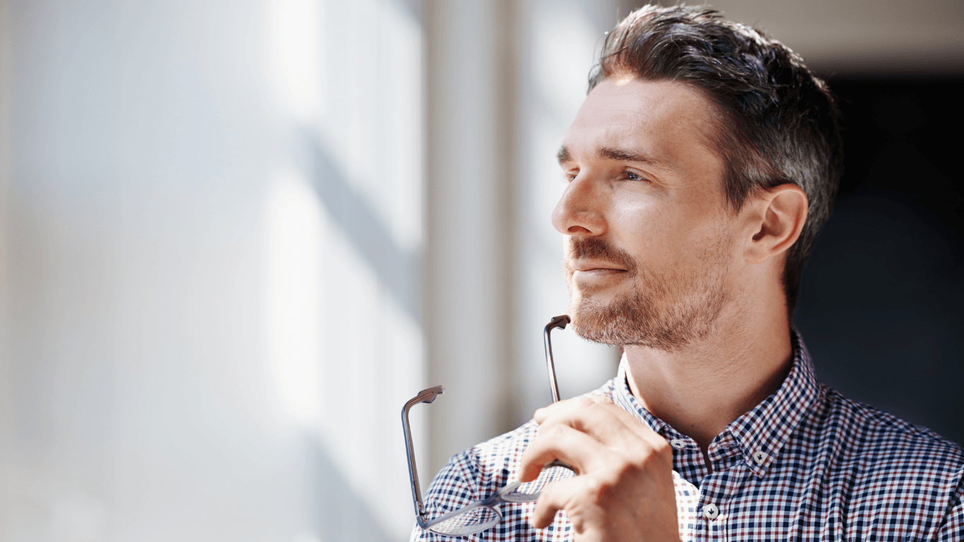 Man Holding Eyeglasses while Looking at the Window